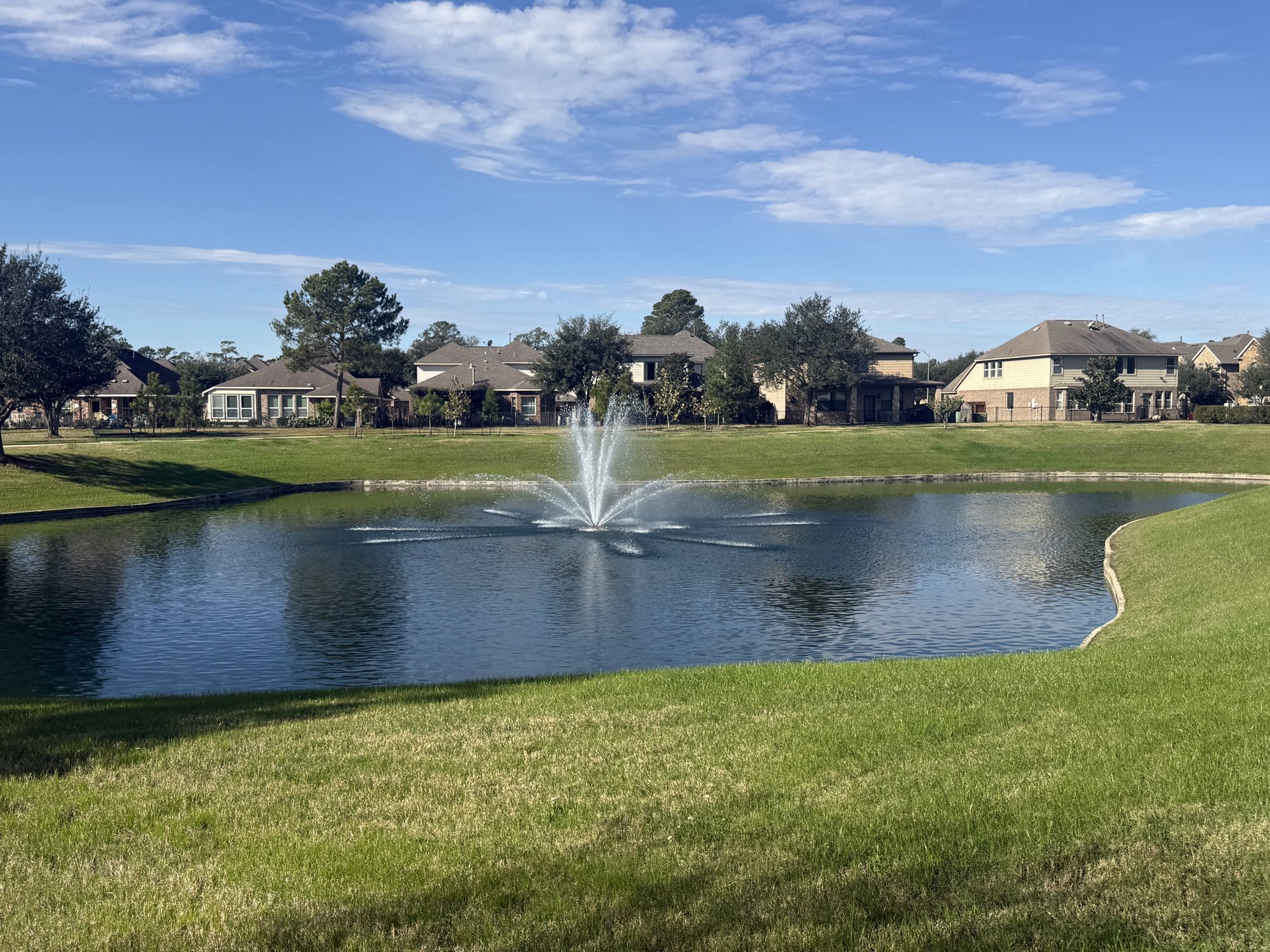 Community pond with aeration fountain running, surrounded by maintained turf